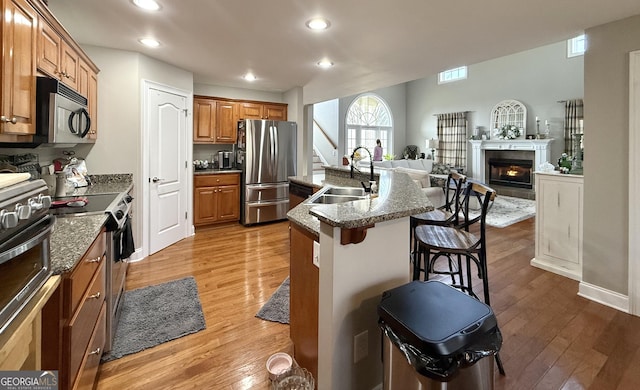 kitchen with brown cabinetry, wood finished floors, stainless steel appliances, a kitchen bar, and a sink