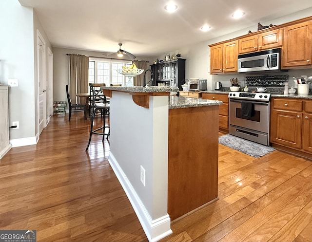 kitchen with light wood finished floors, brown cabinetry, a kitchen breakfast bar, a kitchen island with sink, and stainless steel appliances