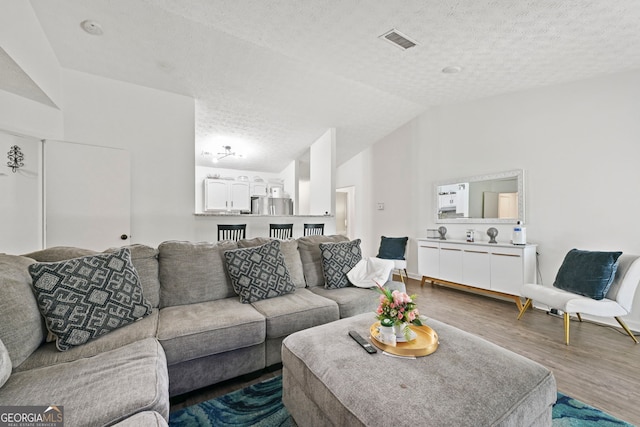 living room with a textured ceiling, visible vents, vaulted ceiling, and wood finished floors