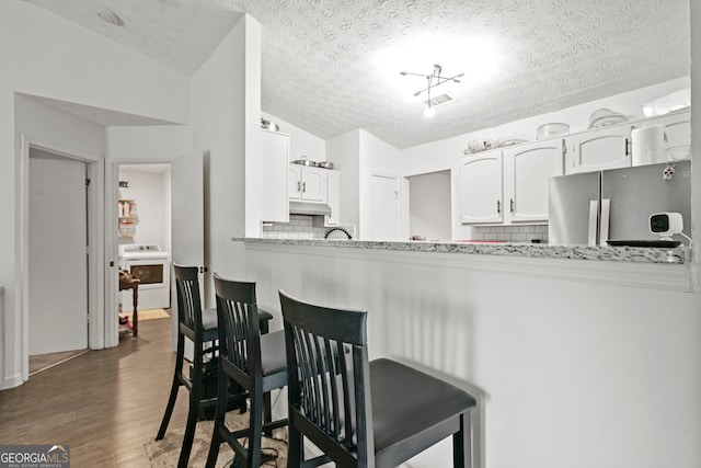 kitchen with washer / dryer, tasteful backsplash, a breakfast bar area, wood finished floors, and freestanding refrigerator