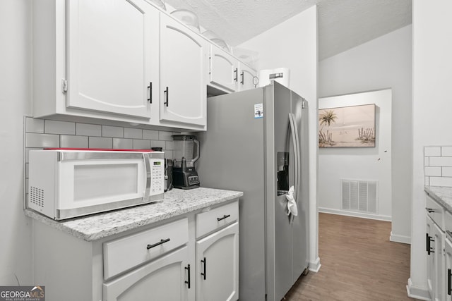 kitchen with white microwave, visible vents, white cabinets, backsplash, and stainless steel fridge