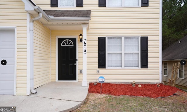 entrance to property with a shingled roof and an attached garage