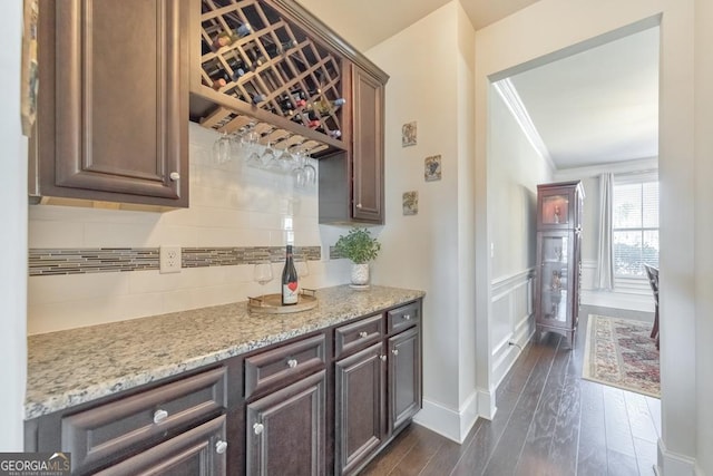 kitchen featuring a wainscoted wall, ornamental molding, tasteful backsplash, dark wood finished floors, and light stone countertops