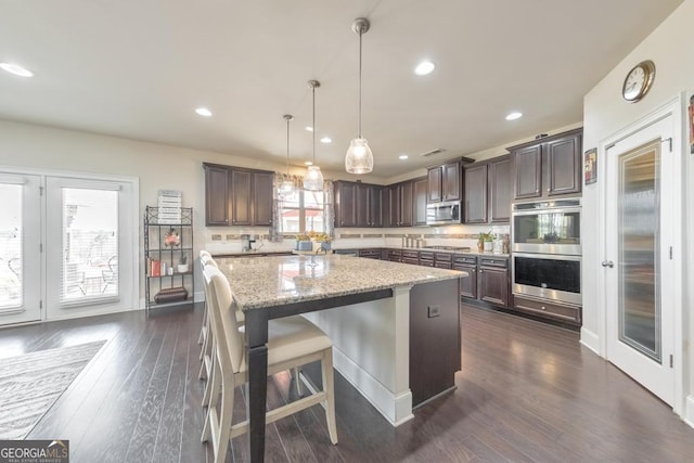 kitchen featuring dark wood-type flooring, light stone counters, a kitchen island, dark brown cabinetry, and appliances with stainless steel finishes