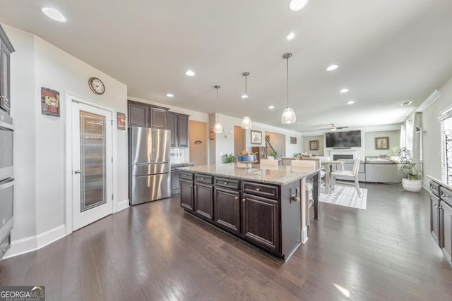 kitchen with open floor plan, appliances with stainless steel finishes, light stone countertops, dark brown cabinets, and dark wood-style flooring