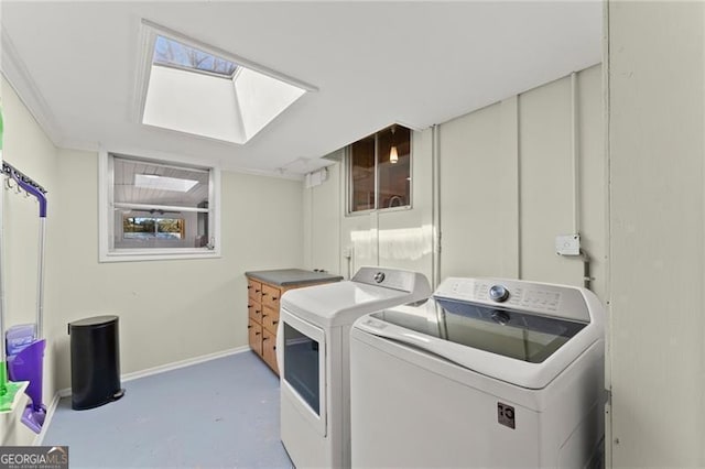 clothes washing area with baseboards, laundry area, a skylight, and washer and dryer