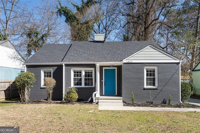 view of front of property with roof with shingles, a front yard, fence, and brick siding