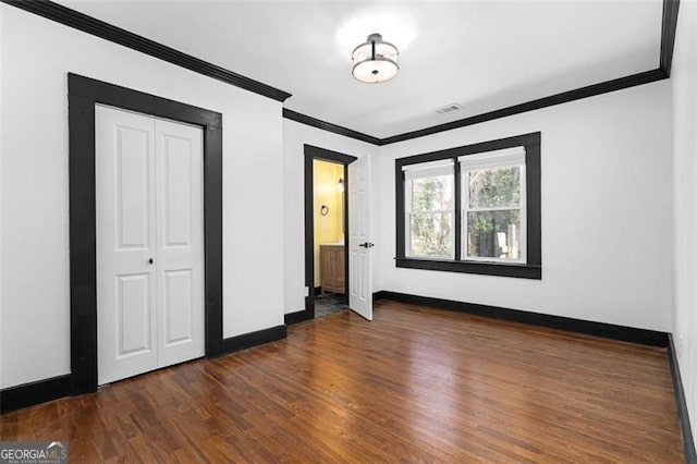 unfurnished bedroom featuring baseboards, visible vents, ornamental molding, dark wood-type flooring, and a closet