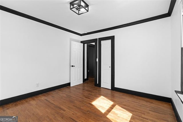 empty room with crown molding, baseboards, and wood finished floors