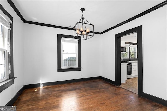 unfurnished dining area featuring dark wood-type flooring, a sink, baseboards, ornamental molding, and an inviting chandelier