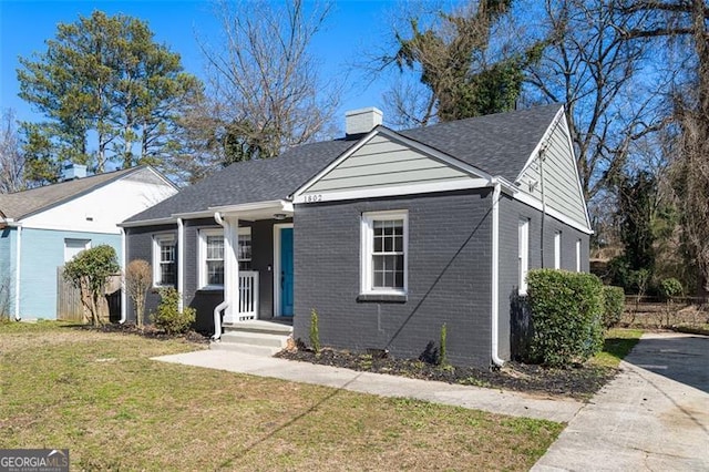 bungalow featuring brick siding, a chimney, and a front yard