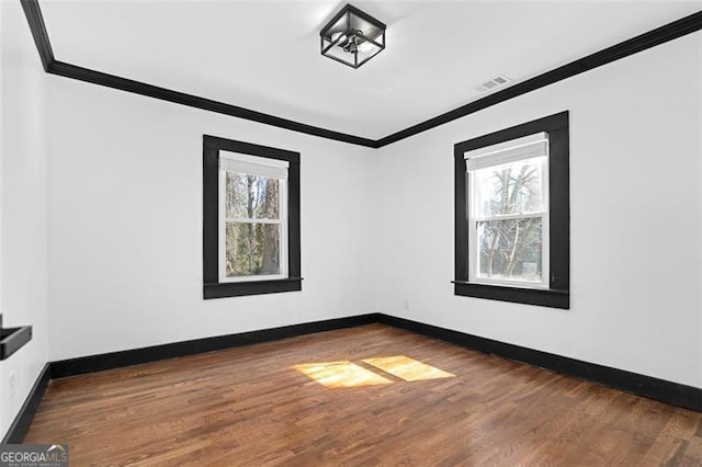 unfurnished room featuring ornamental molding, wood finished floors, visible vents, and baseboards