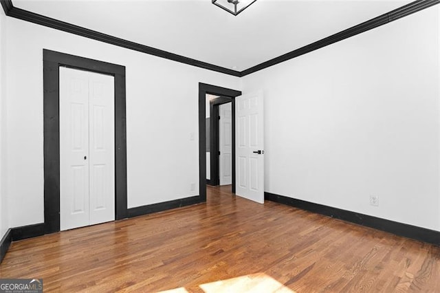 unfurnished bedroom with baseboards, a closet, wood finished floors, and crown molding