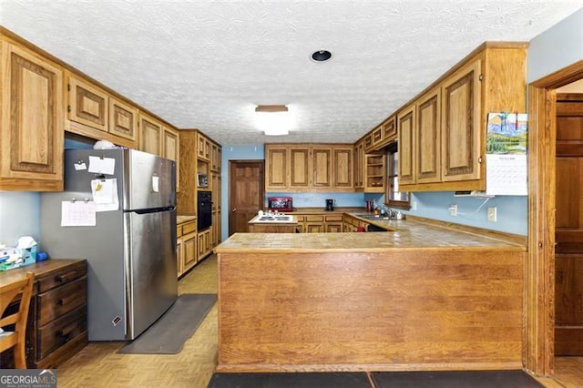 1505 Ozora Rd, Loganville, GA 30052 - kitchen with oven, a peninsula, a sink, freestanding refrigerator, and brown cabinetry