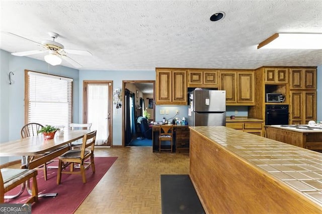 1505 Ozora Rd, Loganville, GA 30052 - kitchen with tile counters, brown cabinetry, oven, freestanding refrigerator, and a textured ceiling