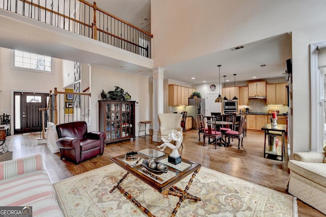 living area with light wood-type flooring, visible vents, decorative columns, and a towering ceiling