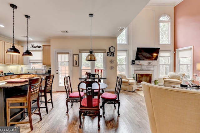 dining area featuring ornamental molding, light wood-type flooring, visible vents, and a premium fireplace