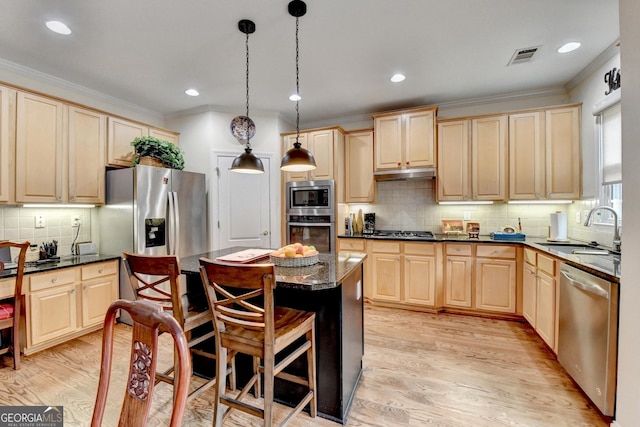 kitchen with a sink, ornamental molding, appliances with stainless steel finishes, light wood-type flooring, and a center island