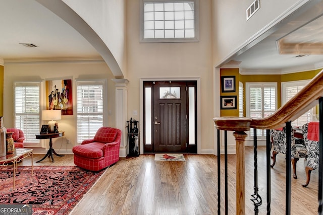 foyer entrance with ornamental molding, stairway, wood finished floors, and visible vents