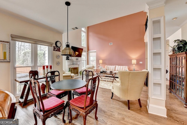 dining area featuring light wood-style flooring, a fireplace, visible vents, and crown molding