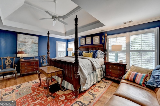 bedroom with a tray ceiling, wood finished floors, visible vents, and a ceiling fan