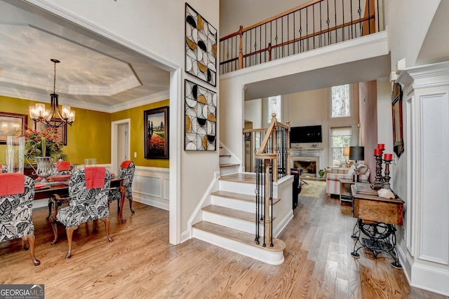 foyer entrance featuring a chandelier, a fireplace, wood finished floors, stairs, and a raised ceiling