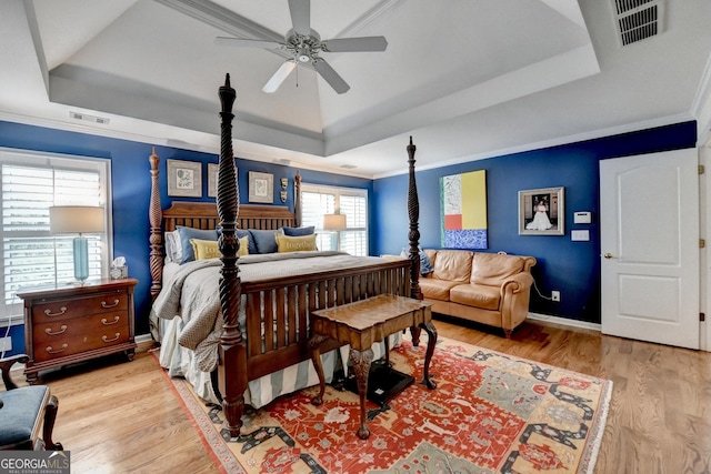 bedroom with baseboards, visible vents, ornamental molding, wood finished floors, and a tray ceiling