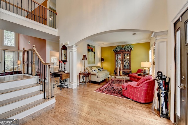 entrance foyer featuring arched walkways, a towering ceiling, stairway, wood finished floors, and crown molding