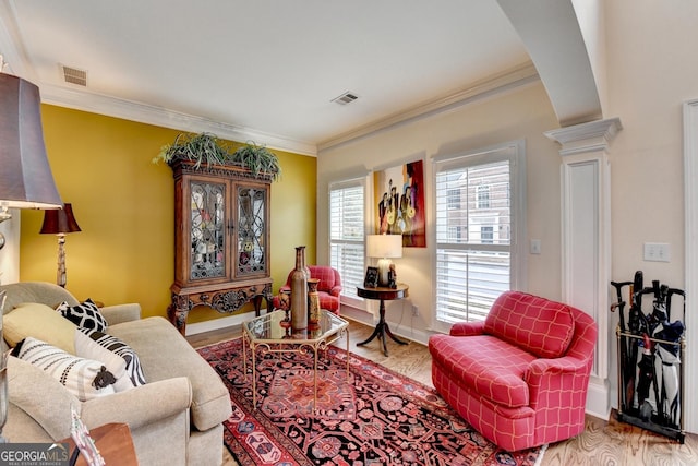 living area featuring decorative columns, crown molding, and wood finished floors