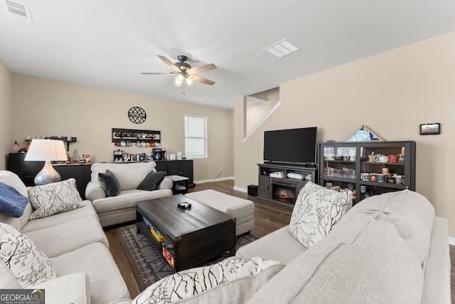 living area with a warm lit fireplace, visible vents, baseboards, a ceiling fan, and wood finished floors