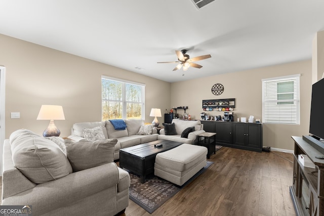 living room with dark wood-style flooring, visible vents, ceiling fan, and baseboards