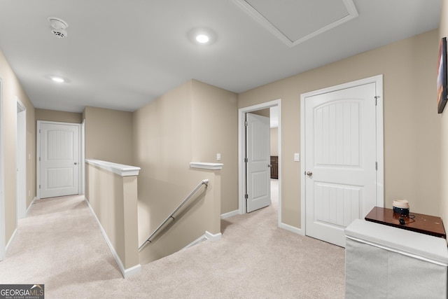 hallway featuring attic access, baseboards, light colored carpet, and an upstairs landing