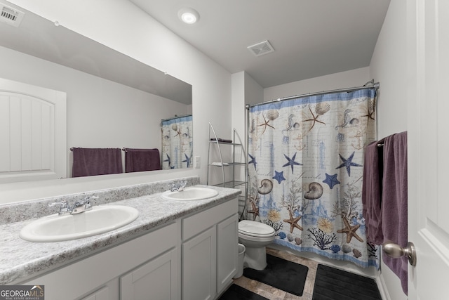 bathroom featuring toilet, double vanity, a sink, and visible vents