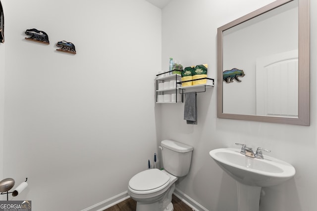 half bath featuring toilet, a sink, baseboards, and wood finished floors