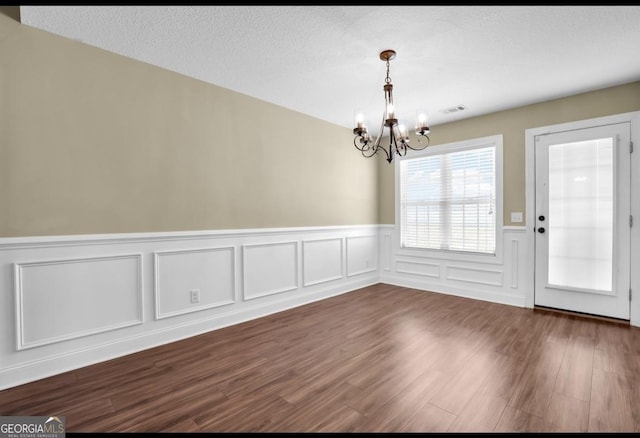 unfurnished dining area featuring a textured ceiling, dark wood-type flooring, visible vents, and an inviting chandelier