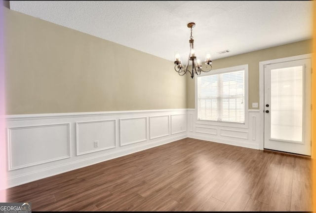 unfurnished dining area with a textured ceiling, visible vents, dark wood finished floors, and a notable chandelier