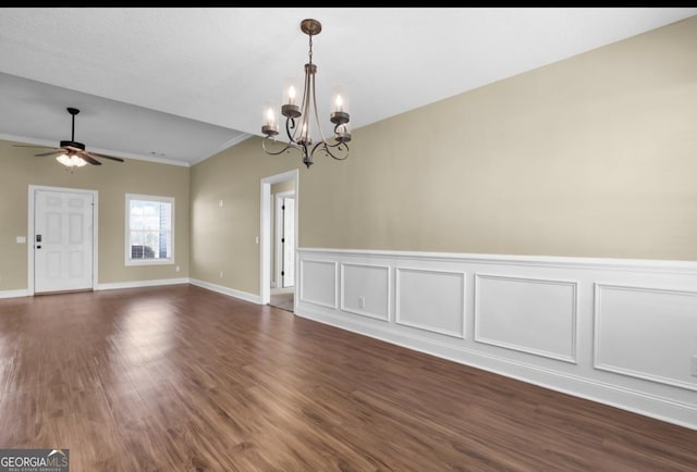 interior space featuring baseboards, dark wood-type flooring, crown molding, a decorative wall, and ceiling fan with notable chandelier