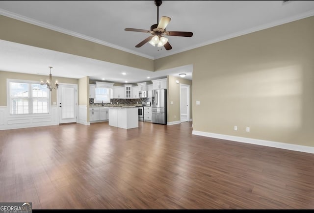 unfurnished living room with dark wood finished floors, ornamental molding, a sink, baseboards, and ceiling fan with notable chandelier