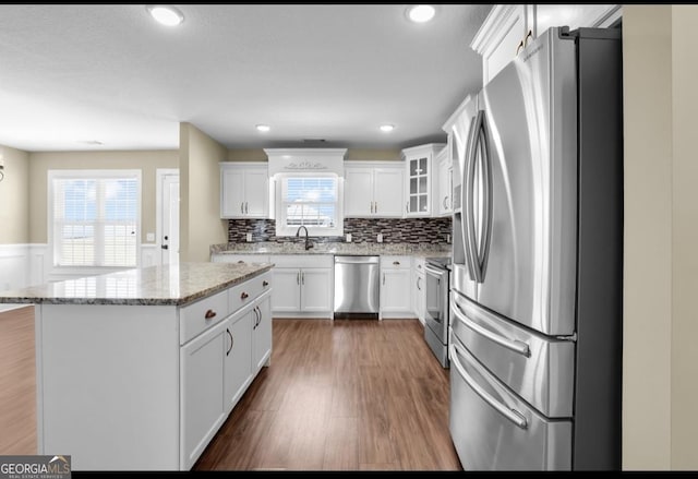 kitchen with a center island, appliances with stainless steel finishes, glass insert cabinets, white cabinets, and wood finished floors