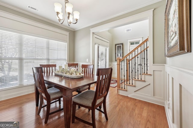 dining space featuring visible vents, ornamental molding, an inviting chandelier, stairs, and light wood-style floors