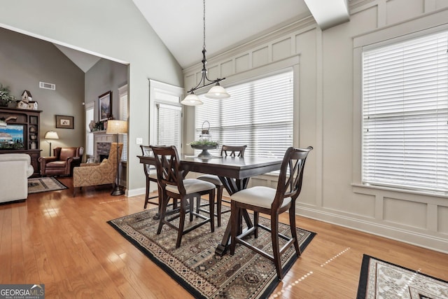 dining space featuring visible vents, light wood-style flooring, a fireplace, high vaulted ceiling, and a decorative wall