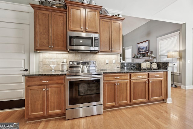 kitchen featuring dark stone counters, appliances with stainless steel finishes, light wood-type flooring, and tasteful backsplash