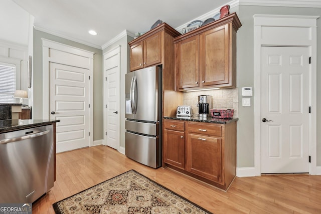 kitchen with decorative backsplash, ornamental molding, dark stone countertops, stainless steel appliances, and light wood-style floors