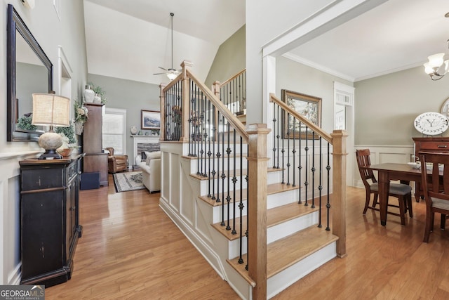 stairway featuring a wainscoted wall, crown molding, a fireplace, vaulted ceiling, and wood finished floors