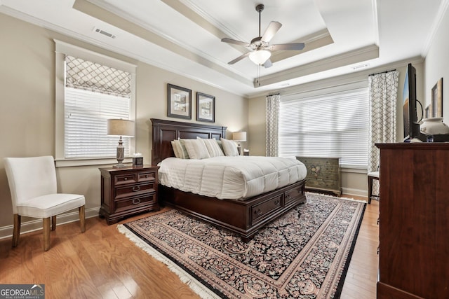 bedroom featuring visible vents, baseboards, a tray ceiling, light wood finished floors, and crown molding