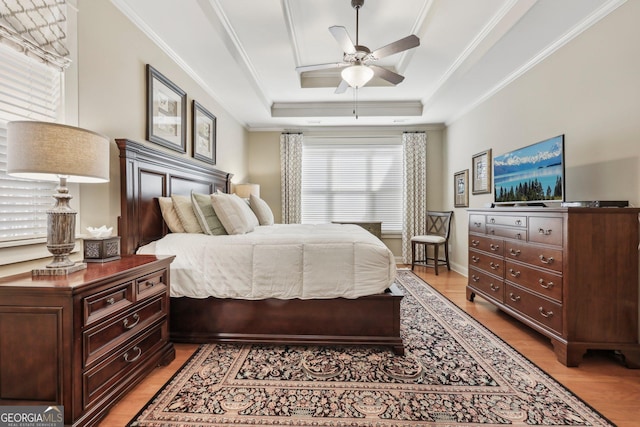 bedroom featuring crown molding, a raised ceiling, light wood-style flooring, a ceiling fan, and baseboards