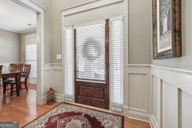 foyer with crown molding, a wainscoted wall, a decorative wall, and light wood-style flooring