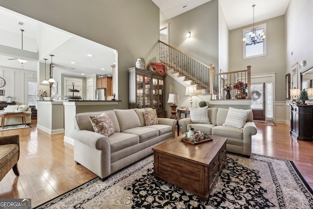 living room with a towering ceiling, stairway, light wood finished floors, and an inviting chandelier