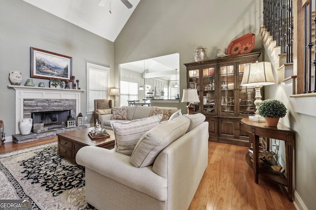 living area featuring high vaulted ceiling, a fireplace, wood finished floors, a ceiling fan, and stairway