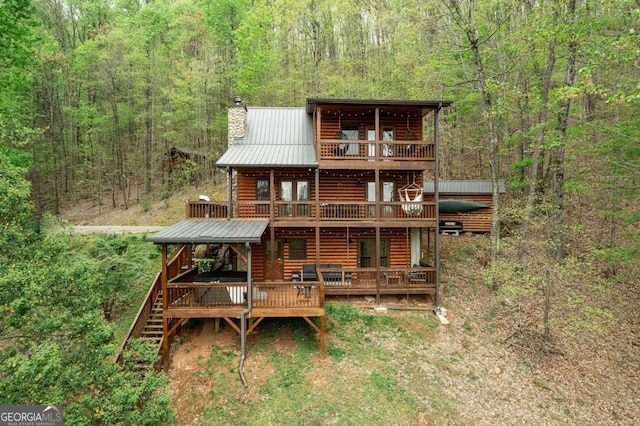 back of property with a chimney, log veneer siding, and a view of trees